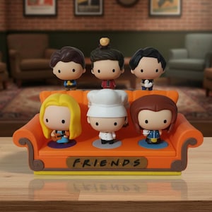 May include: A set of six Friends character figurines. They are displayed on an orange sofa with the word "FRIENDS" on the front. The background shows a living room scene with framed pictures and furniture.