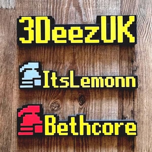 May include: Three pixelated signs with black backgrounds and yellow text are displayed against a wooden background. The top sign reads "3DeezUK", the middle sign says "ItsLemonn", and the bottom sign says "Bethcore". The signs have a retro video game aesthetic.
