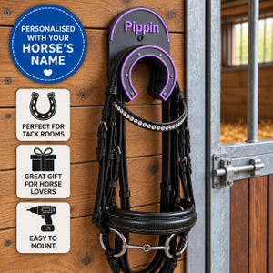 May include: A black horse bridle with a crystal browband hanging on a black and purple wall-mounted rack shaped like a horseshoe. The rack features the name Pippin in purple text. The bridle includes leather straps and a metal bit.