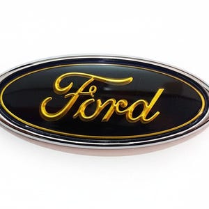 May include: Oval-shaped Ford emblem with a black background and gold script lettering. The emblem is outlined with a silver border. The Ford logo is a classic automotive brand symbol.