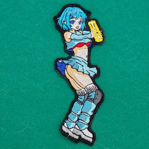 May include: An embroidered patch featuring an anime-style character with bright blue hair, wearing a light blue crop top, a matching pleated skirt, and tall boots. The character holds a yellow cylindrical object in one hand against a black border.