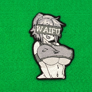 May include: Embroidered patch featuring a stylized anime character with the word "WAIFU" across the eyes. The character is depicted in grayscale with a black outline, set against a green background.
