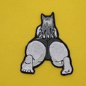 May include: Embroidered patch featuring a cartoon wolf in a kneeling position, with its rear facing the viewer. The wolf is depicted in shades of gray and white, with black outlining the design. The patch is set against a yellow background.