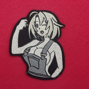 May include: Embroidered patch featuring a stylized anime-style character in overalls, flexing a bicep. The patch is primarily black, white, and gray, with a red background. The character has short, light-colored hair and is winking.
