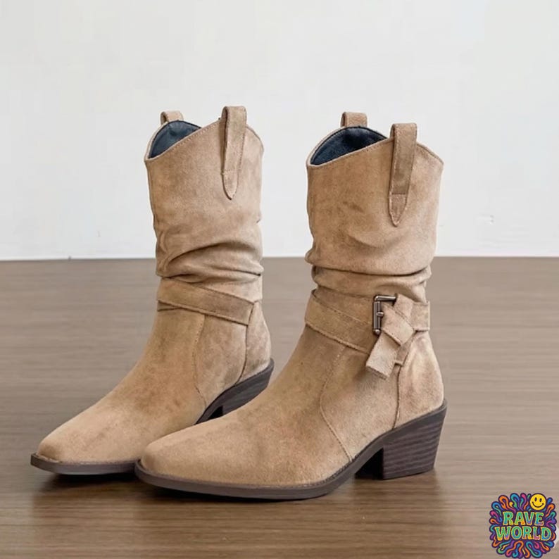 A close-up shot of stylish tan sheepskin and microfiber slouch boots worn at an outdoor music festival. The boots feature a soft, ruched shaft, a pointed toe, and a decorative wrap-around buckle strap. Cream-colored ribbed socks peek out from the top. The background shows a dusty festival ground with a blurred Ferris wheel and crowds under golden hour sunlight, emphasizing a bohemian, desert-chic aesthetic and durable, comfortable design.