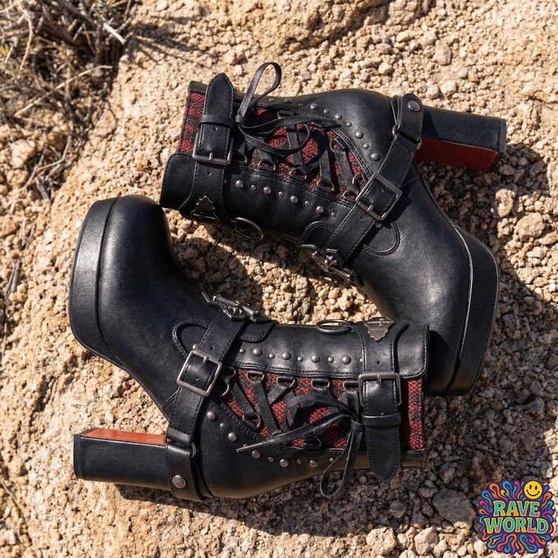 Gemini said
A close-up shot of a person sitting on sun-drenched desert rocks, showcasing edgy black platform ankle boots with chunky high block heels. These gothic-inspired boots feature multiple silver buckles, decorative straps, and eye-catching red mesh detailing along the sides. They boast a thick platform sole and a distinct red contrast on the rear of the heel. The person wears black distressed skinny jeans against a vast and rugged desert environment.