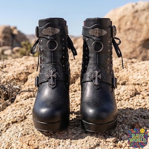 Gemini said
A close-up shot of a person sitting on sun-drenched desert rocks, showcasing edgy black platform ankle boots with chunky high block heels. These gothic-inspired boots feature multiple silver buckles, decorative straps, and eye-catching red mesh detailing along the sides. They boast a thick platform sole and a distinct red contrast on the rear of the heel. The person wears black distressed skinny jeans against a vast and rugged desert environment.