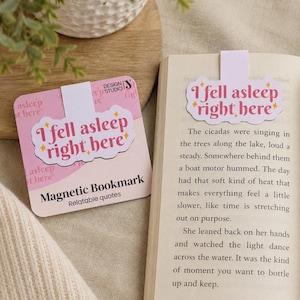 Op de afbeelding: Roze magnetische boekenlegger met de tekst "I fell asleep right here" in een wolk, met gouden sterren. De boekenlegger ligt op een boek. De woorden "Magnetic Bookmark Relatable quotes" zijn ook zichtbaar.