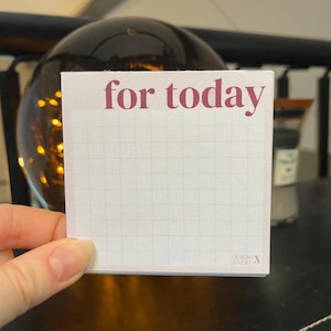 Peut inclure: Un petit bloc-notes carré avec un fond rose clair et un motif quadrillé. Les mots "for today" sont imprimés en bordeaux en haut. Le bloc-notes est tenu par une main.