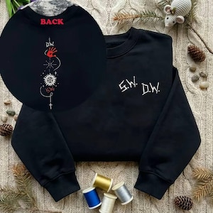 Może przedstawiać: Czarna bluza z białym haftowanym tekstem "S.W. D.W." z przodu. Tył posiada czerwony napis "BACK" przy dekolcie oraz szczegółowy biało-czerwony haftowany wzór.