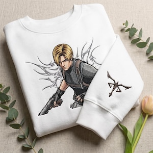 Könnte beinhalten: Weißes Sweatshirt mit einer Stickerei eines Charakters mit blonden Haaren, der eine Waffe hält. Der Charakter trägt eine schwarze taktische Weste. Auf dem Ärmel befindet sich ein braunes Emblem.