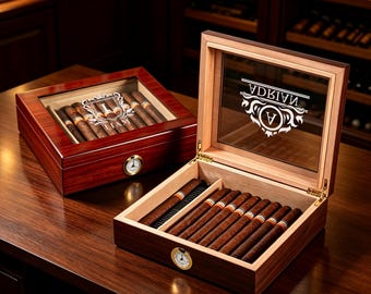 Può includere: Due humidor per sigari rettangolari in legno con coperchi in vetro. Uno è chiuso, con il nome LIAM e uno stemma. L'altro è aperto, rivelando sigari e un igrometro, con il nome ADRIAN e uno stemma stampati sul coperchio in vetro.