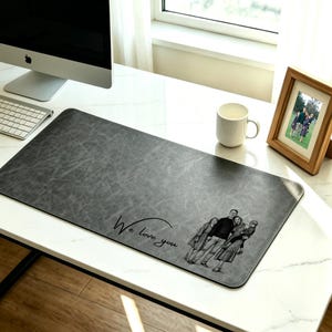 May include: Gray rectangular desk mat with a textured surface. The mat features a family portrait and the text "We love you" in a script font. A white mug and a framed photo are also on the desk.
