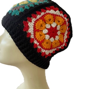 May include: A black crocheted beanie hat with a colourful floral design. The hat features a central pattern of red, orange, and white, surrounded by a black border. The top of the hat has a pattern of teal, yellow, and brown.