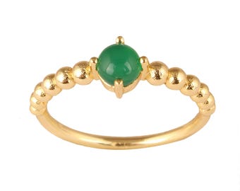 Puede incluir: Anillo dorado con una gema verde redonda en el centro. La banda está adornada con pequeñas cuentas doradas espaciadas uniformemente. La gema verde está sujeta por cuatro garras.
