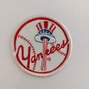 May include: Embroidered circular patch with the New York Yankees logo. The design features a baseball with red stitching, the word "Yankees" in red script, and an Uncle Sam hat. The patch has a red and white stitched border.
