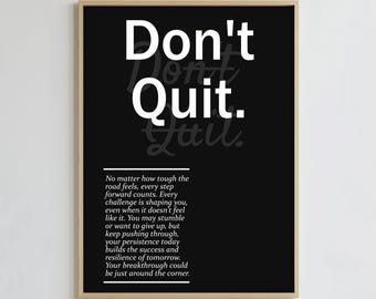 May include: A framed black and white print with the words "Don't Quit" in large white letters. Below the text is a motivational quote about perseverance. The frame is a light brown color.