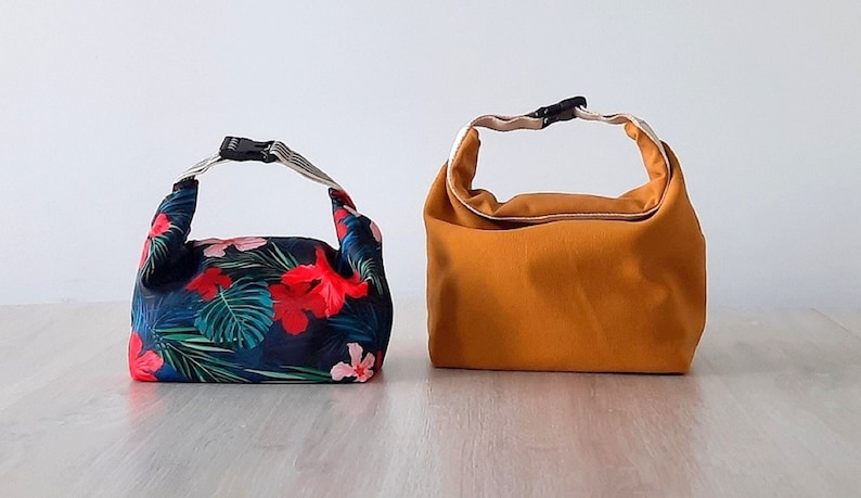May include: Two lunch bags, one with a tropical floral print and the other a solid mustard yellow.