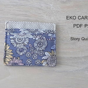 May include: A gray card wallet with a floral pattern in shades of yellow, pink, and white. The text "EKO CARD WALLET PDF PATTERN Story Quilt Etsy Shop" is printed above the wallet.