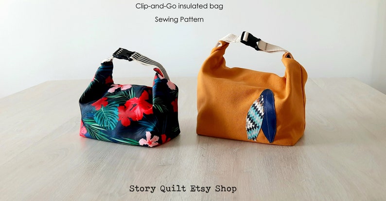 May include: Two insulated lunch bags, one with a tropical floral print and the other with a solid orange fabric and a blue and white geometric design. The bags have a clip-and-go closure and are made for carrying lunches or snacks. "Story Quilt Etsy Shop" is printed on the table below the bags.