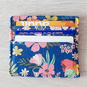 May include: A blue fabric card holder with a floral pattern. The holder has three slots for cards and is filled with cards.