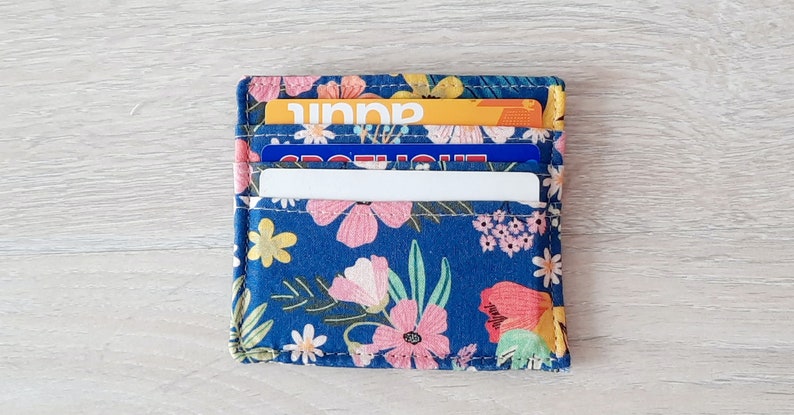 May include: A blue fabric card holder with a floral pattern. The holder has three slots for cards and is filled with cards.