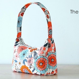 May include: A white fabric handbag with a floral print in shades of orange, pink, and blue. The bag has a single top handle.