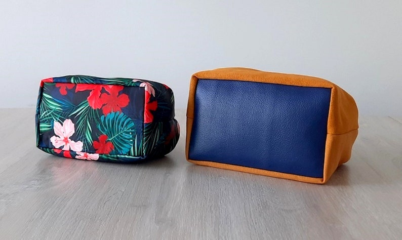 May include: Two rectangular fabric bags. One bag is blue with a tropical floral print. The other bag is blue with a solid orange border.