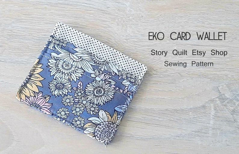 May include: A blue and white floral fabric card wallet with a white polka dot fabric lining. The wallet is folded in half and is lying on a light wood surface. The text "EKO CARD WALLET" and "Story Quilt Etsy Shop Sewing Pattern" is printed above the wallet.