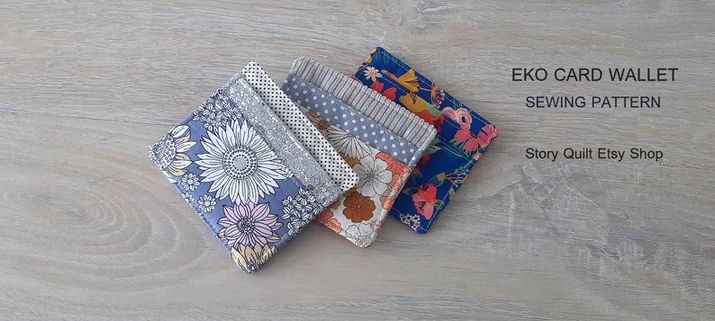 May include: Four different fabric card wallet sewing patterns with floral designs. The patterns are folded and stacked on a light wood surface. The text "EKO CARD WALLET SEWING PATTERN Story Quilt Etsy Shop" is printed on the surface.