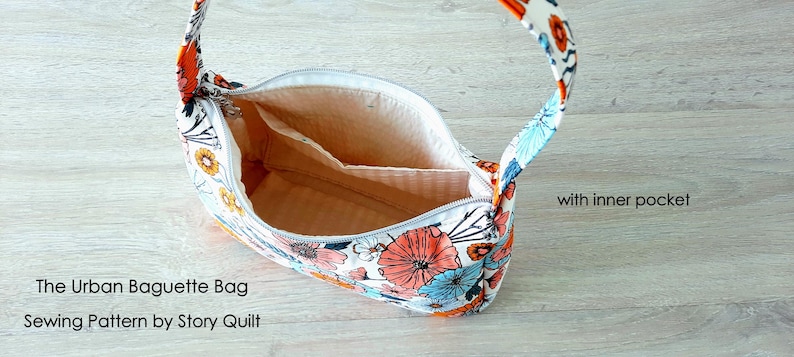 May include: A white fabric bag with a floral print in shades of orange, blue, and white. The bag has a single strap and a zipper closure. The bag is open and the inside is lined with a beige fabric. The bag has an inner pocket. The text "The Urban Baguette Bag Sewing Pattern by Story Quilt" is visible at the bottom of the image.