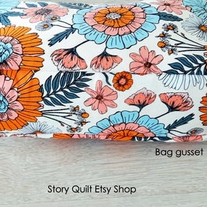 May include: Close-up of a white fabric bag with a floral print in shades of orange, pink, and blue. The bag has a gusset and the text "Story Quilt Etsy Shop" is visible at the bottom of the image.