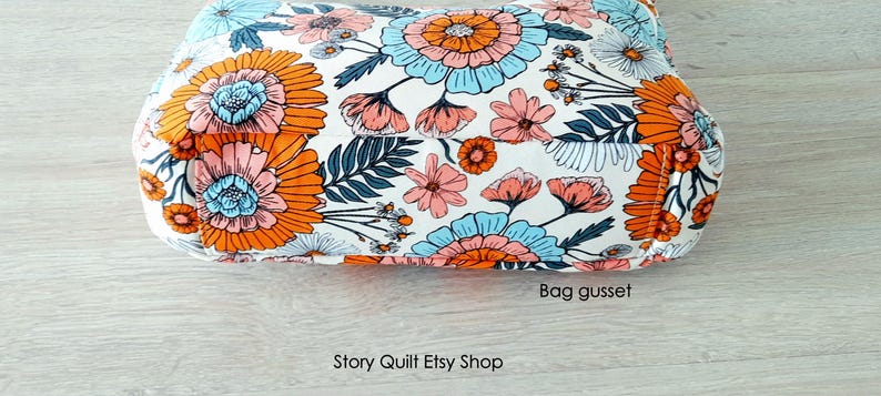 May include: Close-up of a white fabric bag with a floral print in shades of orange, pink, and blue. The bag has a gusset and the text "Story Quilt Etsy Shop" is visible at the bottom of the image.