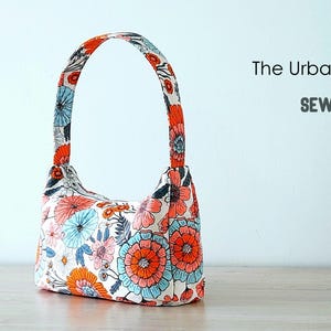 May include: A white fabric handbag with a floral print in shades of orange, pink, and blue. The bag has a single top handle and a curved shape. The text "The Urban Baguette" and "Sewing Tutorial" is visible in the image.