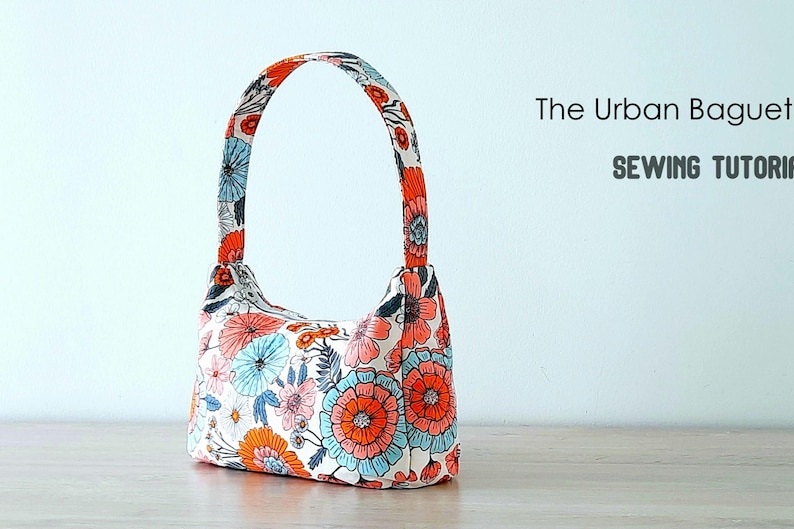 May include: A white fabric handbag with a floral print in shades of orange, pink, and blue. The bag has a single top handle and a curved shape. The text "The Urban Baguette" and "Sewing Tutorial" is visible in the image.