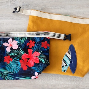 May include: Two reusable shopping bags. One bag is yellow with a blue and white surfboard design. The other bag is black with a tropical floral print featuring pink and red flowers.