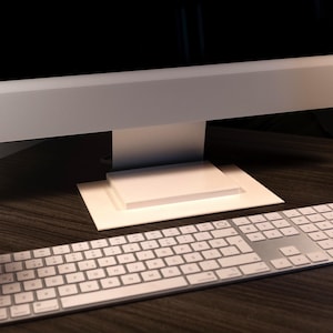 May include: A modern computer setup featuring a silver keyboard with white keys and a large monitor. The monitor is white with a black screen, and the keyboard is positioned in front of it on a dark wooden desk.