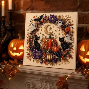 May include: A square diamond painting canvas featuring a Halloween wreath design with two black cats, white ghosts, orange pumpkins, a crescent moon, and a lantern. The artwork is embellished with colorful beads and sequins on a light background.