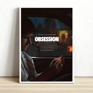 May include: A framed movie poster for "Obsession" featuring a man in a car, with the title in large letters. The poster includes the text "Be careful who you wish for..." and "Only in theaters May 15."