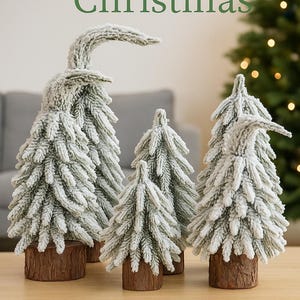 Pode incluir: Uma coleção de figuras decorativas de árvores de Natal. As árvores são cobertas com flocagem branca e têm bases castanhas. O texto "Merry Christmas" está no topo. As árvores estão numa mesa de madeira.