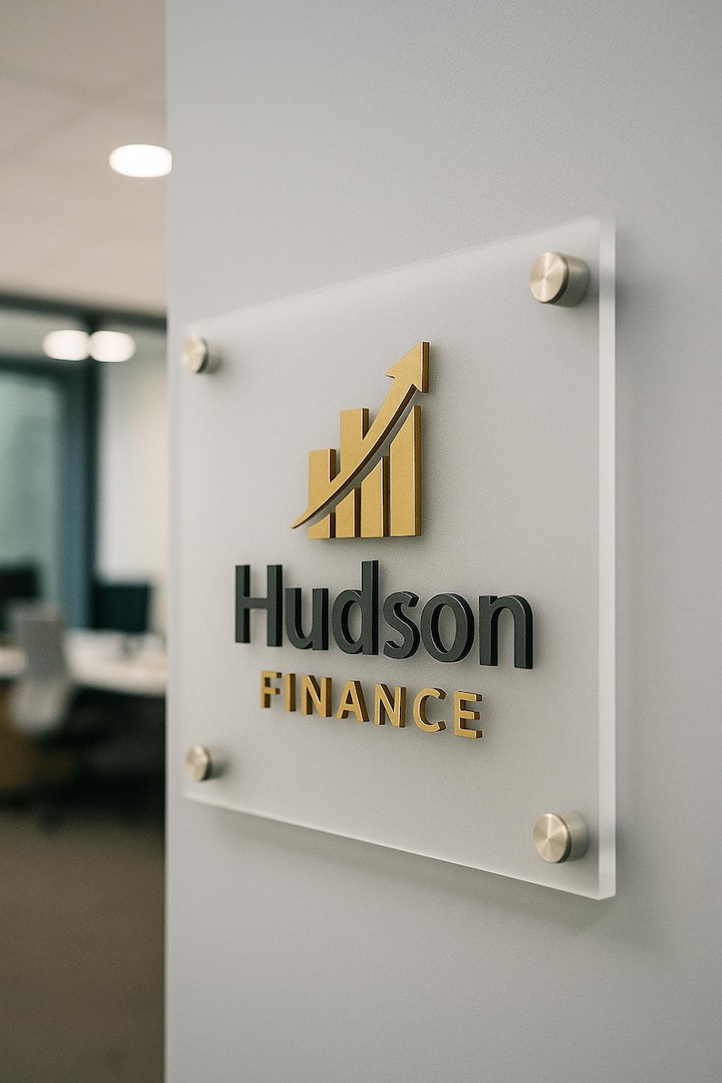 Puede incluir: Un letrero de acr&iacute;lico transparente con el logotipo de Hudson Finance. El logotipo presenta una flecha y barras doradas que apuntan hacia arriba, con el nombre "Hudson" en negro y "Finance" en dorado. El letrero est&aacute; fijado a una pared gris.