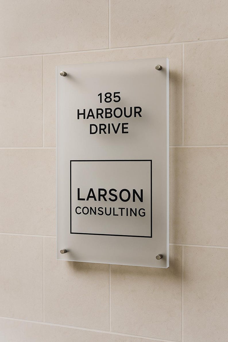 Puede incluir: Un letrero de vidrio esmerilado con la direcci&oacute;n "185 HARBOUR DRIVE" y el nombre "LARSON CONSULTING" en letras negras. El letrero est&aacute; montado en una pared de azulejos beige con cuatro separadores plateados.