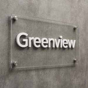 Puede incluir: Un letrero rectangular de acr&iacute;lico transparente con la palabra "Greenview" en blanco. El letrero est&aacute; montado en una pared de hormig&oacute;n gris con cuatro separadores plateados.