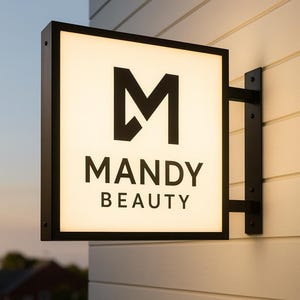 Może przedstawiać: Kwadratowy, podświetlany szyld z czarną ramą i wspornikiem, zamontowany na białej ścianie. Szyld wyświetla czarny tekst "MANDY BEAUTY" ze stylizowanym logo "M". Szyld jest podświetlany od wewnątrz.