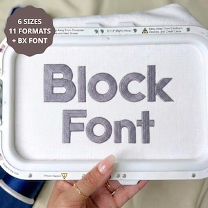 May include: A white embroidery hoop frame containing white fabric with the grey embroidered text Block Font. The frame features printed text including 8x13 Mighty Hoop and safety warnings. A brown circular graphic overlay displays 6 SIZES 11 FORMATS + BX FONT.