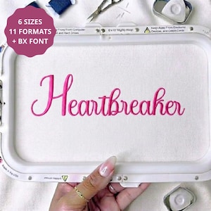 May include: A white embroidery hoop frame containing white fabric with the word Heartbreaker stitched in bright pink cursive thread. A pink circular graphic in the top left corner displays the text 6 SIZES 11 FORMATS + BX FONT.