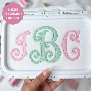 May include: An embroidery hoop containing white fabric with the stitched monogram letters I, B, and C. The letters I and C are pink, while the letter B is light green. A pink circular graphic overlay displays the text 6 SIZES, 11 FORMATS, + BX FONT.