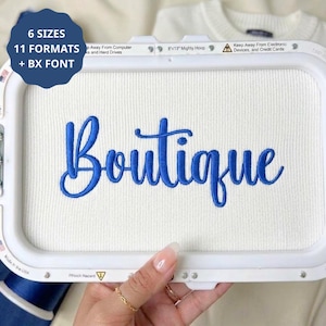 以下が含まれることがあります： 白い刺繍枠に白い布が張られ、青い糸でBoutiqueという文字が刺繍されています。左上の濃い青色の円形バッジには、6 SIZES 11 FORMATS + BX FONTというテキストが表示されています。枠のサイズは20.32x33.02 cmです。