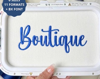 Op de afbeelding: Een witte borduurring met witte stof waarop het woord Boutique met blauwe draad is geborduurd. Een donkerblauwe ronde badge in de linkerbovenhoek toont de tekst 6 SIZES 11 FORMATS + BX FONT. Het frame meet 20,32x33,02 cm.