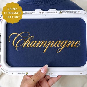 Puede incluir: Un bastidor de bordado blanco que sostiene una tela azul oscuro con la palabra Champagne bordada en hilo dorado. Una insignia circular amarilla en la esquina superior izquierda muestra el texto 6 SIZES 11 FORMATS + BX FONT. El marco incluye textos de seguridad.